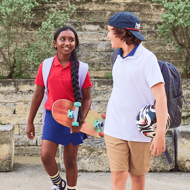 Two students in school uniform outfits walking outside with backpacks.