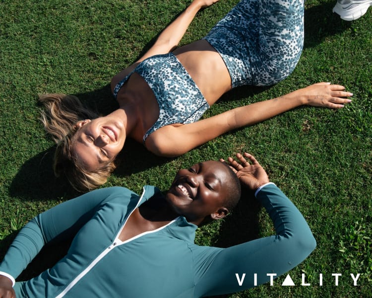 Two people wearing blue patterned and solid blue activewear while lying on grass, with VITALITY logo.