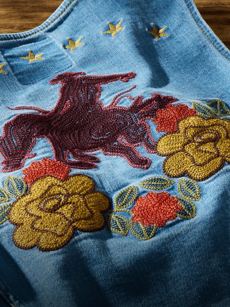 Close-up of an embroidered Lainey Wilson X Wrangler denim vest featuring a rodeo rider and floral designs in red, yellow, and orange.