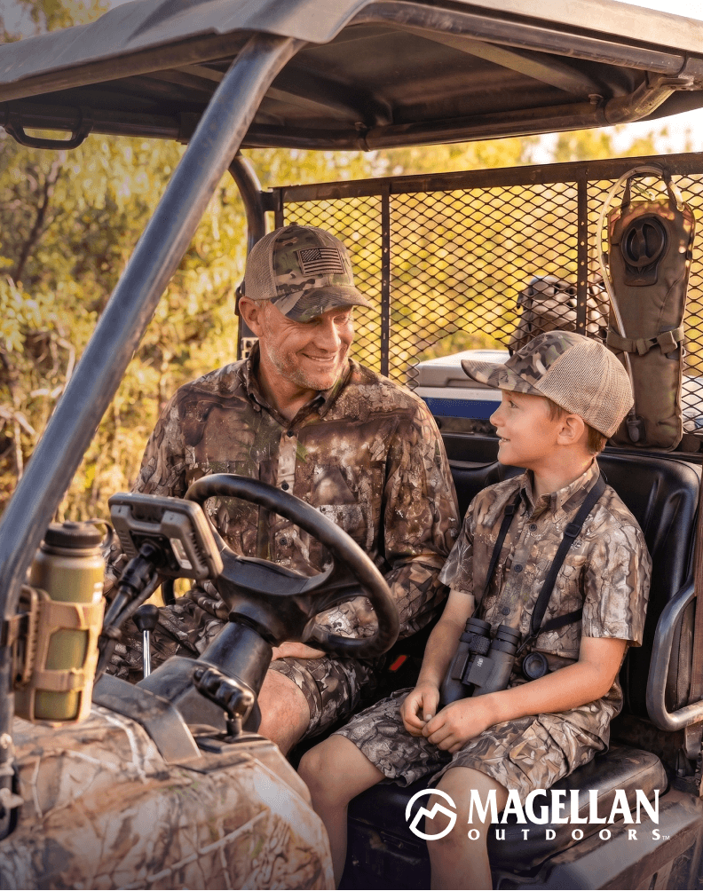 Two people wearing camouflage apparel seated in a utility vehicle outdoors.