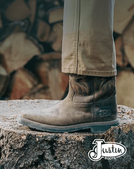 Worn leather Justin work boots standing on a cut tree stump in an outdoor work setting.