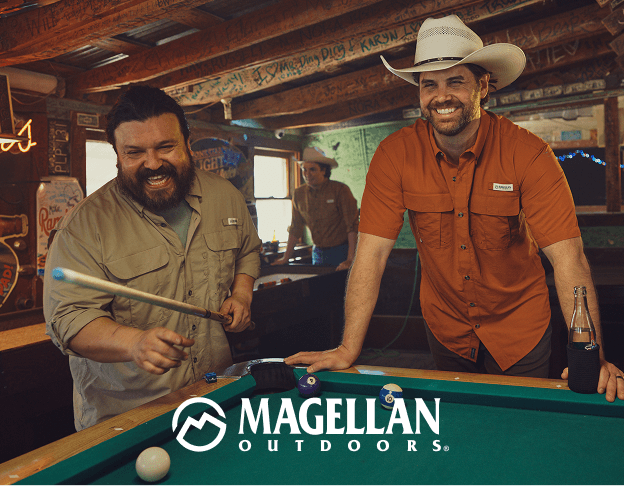 Two people wearing outdoor apparel inside a rustic workshop with Magellan Outdoors branding.