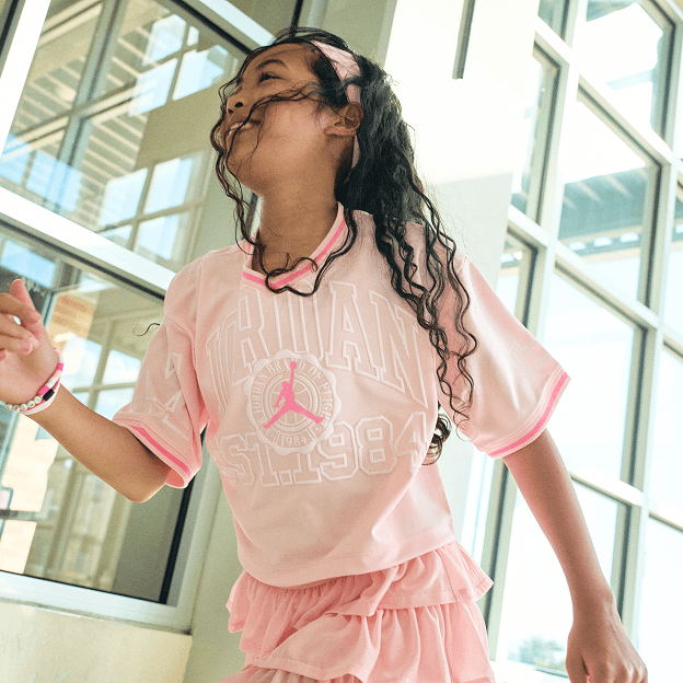 Kid wearing pink outfit with backpack walking near school building.