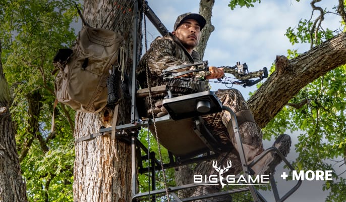 Hunter seated in an elevated tree stand holding a crossbow among large trees.
