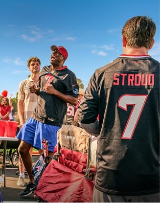 Football fans wearing NFL team jerseys in a stadium-style setting.