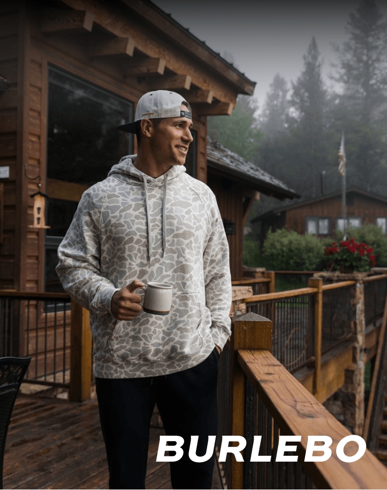 Person wearing a BURLEBO gray pullover sweatshirt while standing outdoors near a cabin deck.