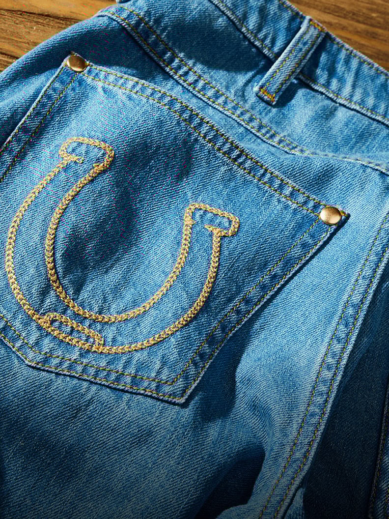 Close-up of a denim back pocket of Lainey Wilson X Wrangler embroidered cowboy shorts featuring a stitched horseshoe design.