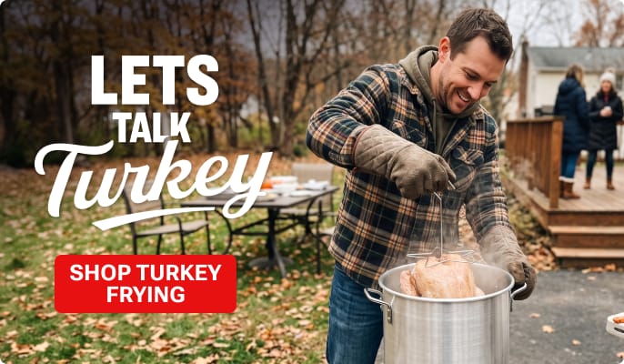 Person lowering a turkey into a large outdoor frying pot in a backyard with autumn trees and family gathering in the background. Promotional text reads: LETS TALK Turkey. Red button reads: SHOP TURKEY FRYING.