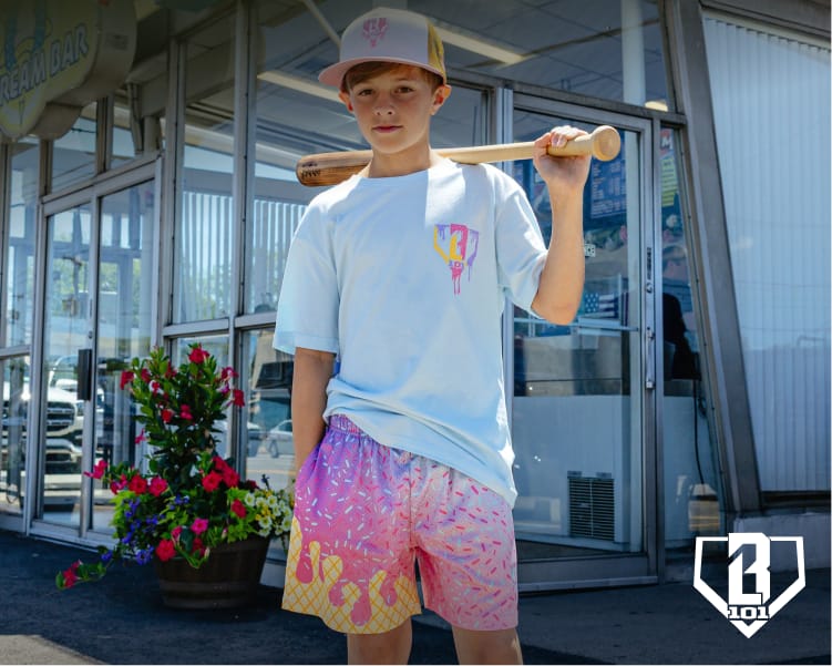 Child standing outside a storefront holding a baseball bat while wearing a white graphic T-shirt and colorful shorts from the Ice Cream Collection, with Baseball Lifestyle 101 logo overlay.