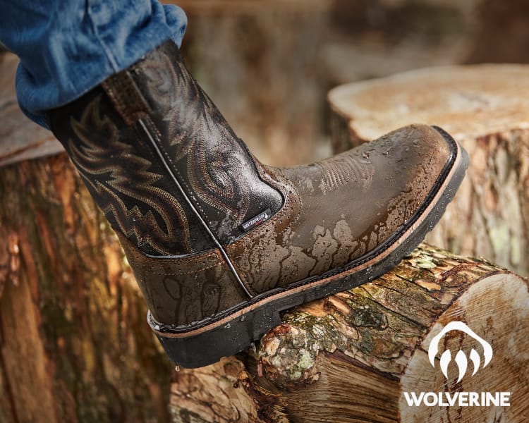 Mud-covered Wolverine work boot resting on a log with CAT and Wolverine overlaid brand logos.