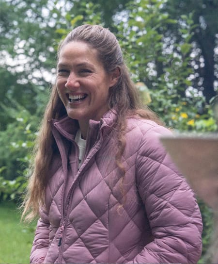 Person standing outdoors in a garden wearing a mauve quilted jacket.
