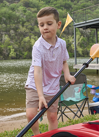 Outdoor lakeside scene showing a young person wearing BURLEBO holding a kayak paddle near the water.
