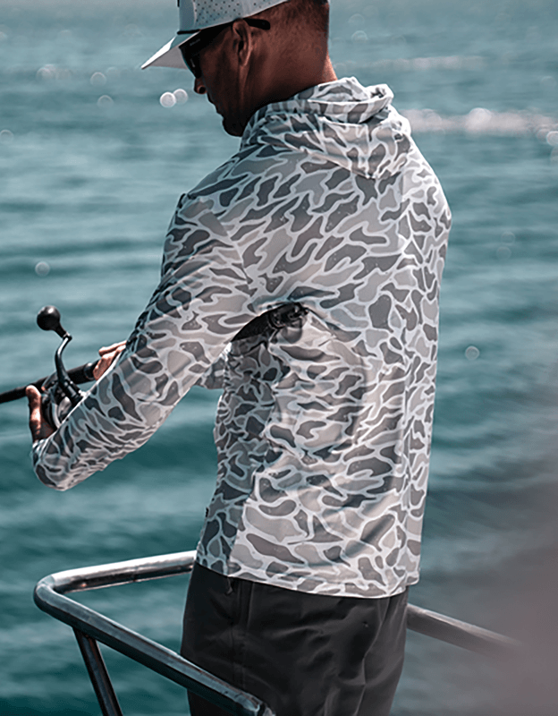 Rear view of person wearing a gray camo performance hoodie near water outdoors.