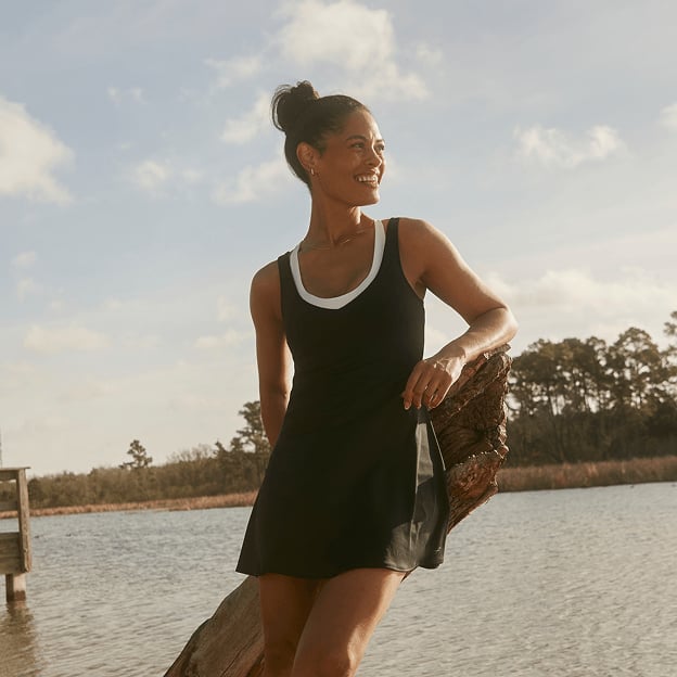 Person standing by a lakeside wearing a sleeveless black athletic dress from FREELY.