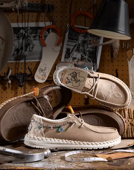 Pair of brown HEYDUDE x Rodeo shoes with western-style stitching and orange lace tips.