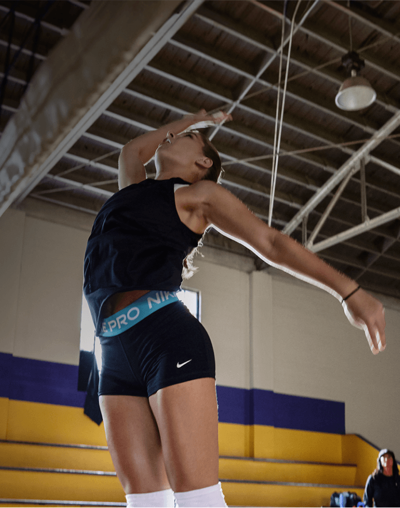 Player jumping at a volleyball net in an indoor gym during a game.