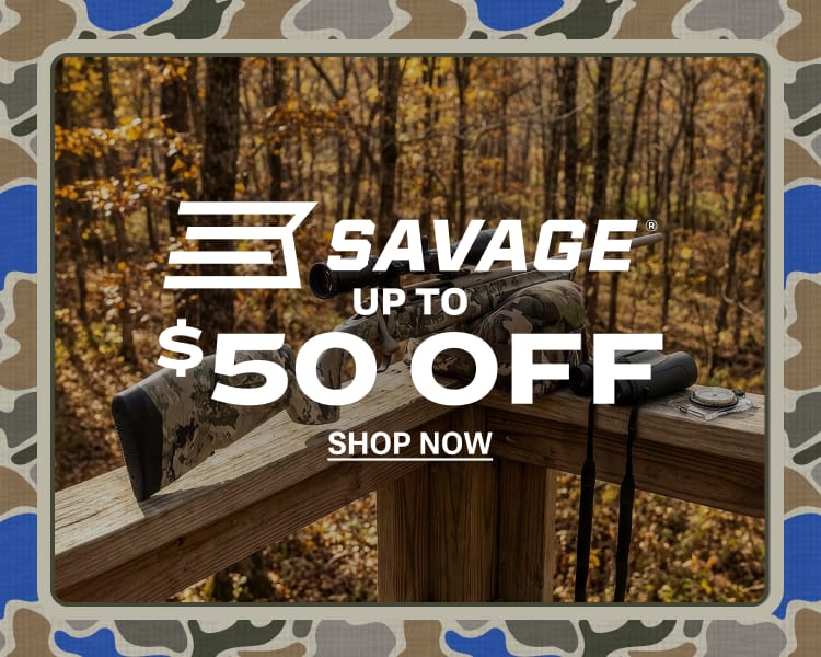 Savage rifle with mounted scope resting on a wooden shooting bench in a wooded outdoor setting.