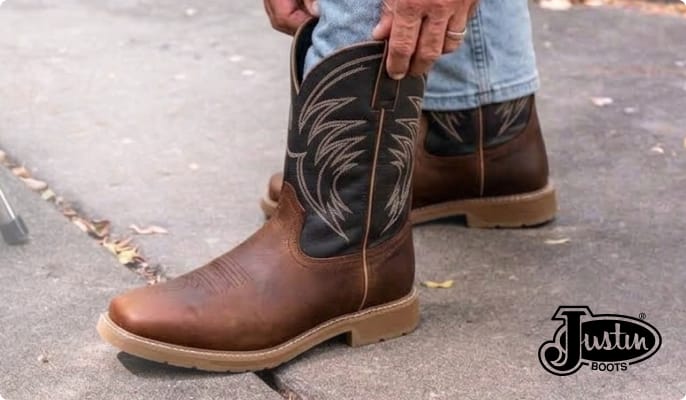 Close-up of a person pulling on a brown leather Justin Boots western work boot while wearing jeans.