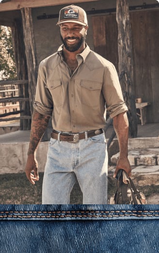 Two men wearing Western-style shirts, belts, and jeans walking outdoors near a rustic wooden building.