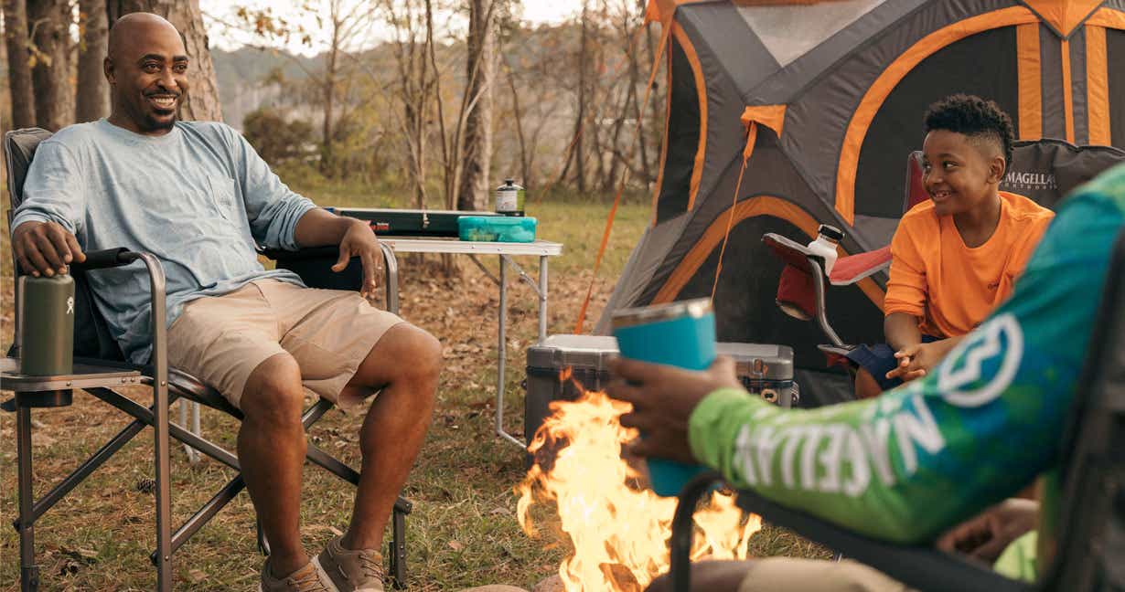 Man in front of a camping tent entertains his children by their campsite fire