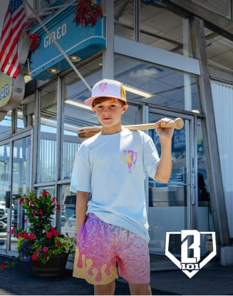 Model wearing colorful casual Baseball Lifestyle 101 apparel and holding a skateboard in front of a retail storefront.