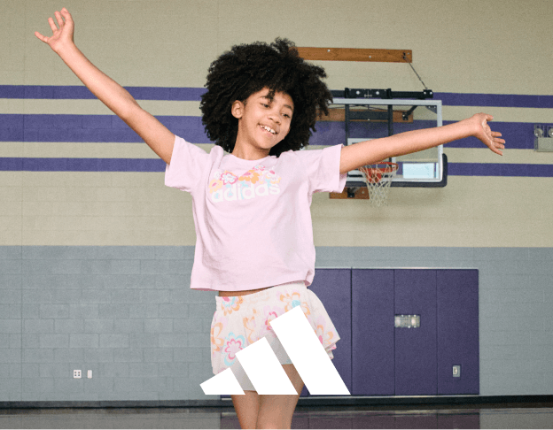 Person in a pink top and white skirt posing with arms extended in a gymnasium. adidas