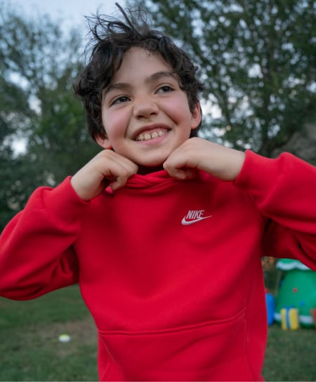 Child outdoors wearing a red Nike hoodie with hands at the collar.