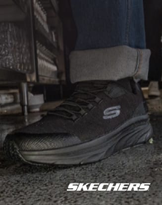 Close-up of a black Skechers work shoe on a wet industrial floor with rolled-up pant cuffs visible.