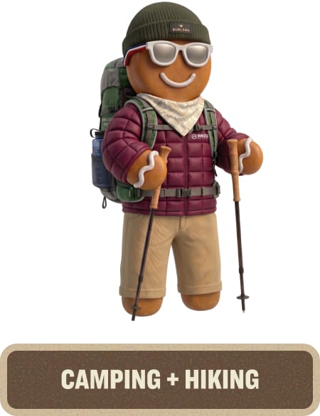 Gingerbread character wearing outdoor apparel with a backpack, sunglasses, and hiking poles. Text below reads “Camping + Hiking.”