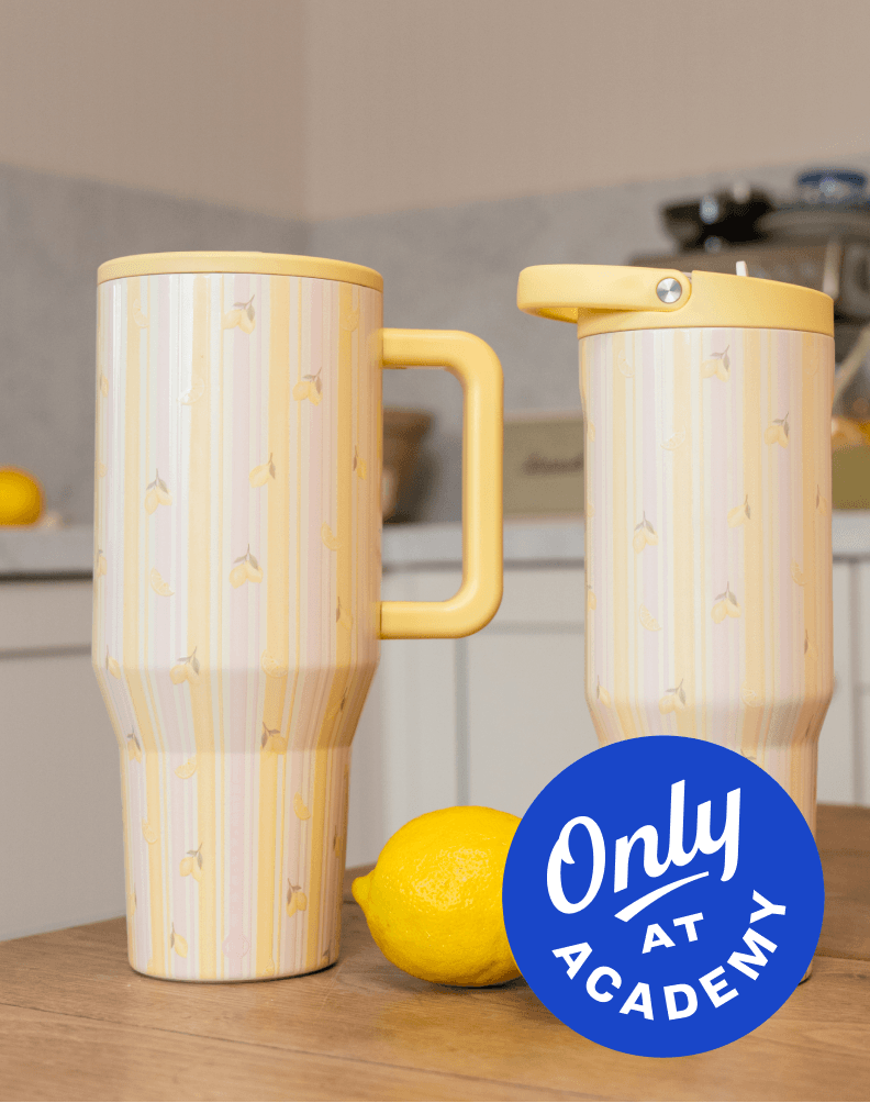 Two large handled tumblers with lids in pink lemonade color placed on a kitchen counter beside lemons, with text Only at Academy.