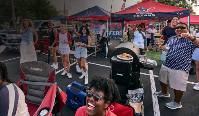Fans enjoy a tailgate party with grilling, lawn games, camping gear, and an H-Town Tailgaters banner.