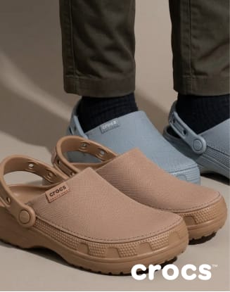 Tan Crocs clogs displayed in front of a person wearing gray Crocs footwear.