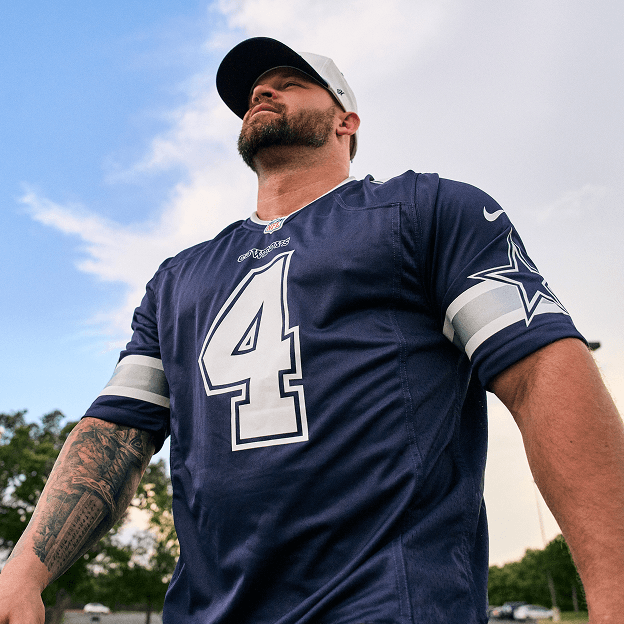 Person wearing a Dallas Cowboys jersey standing outdoors against a blue sky.