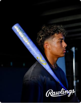 Athlete holding a blue Rawlings baseball bat over one shoulder in a dark indoor setting. Rawlings logo appears at the bottom.