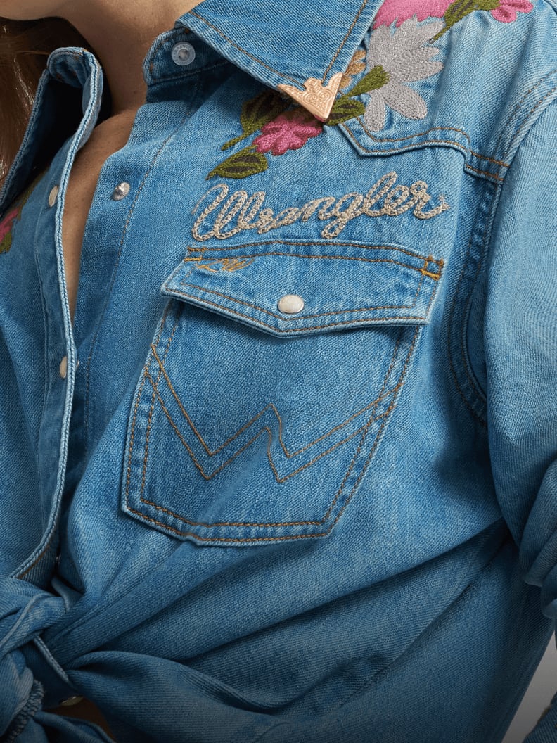 Close-up of a Lainey Wilson X Wrangler light-wash embroidered denim shirt with floral stitching on the collar and the Wrangler logo on the chest pocket.