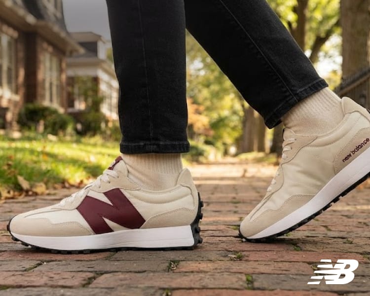 Cream and burgundy New Balance sneaker worn with black pants on a brick walkway, with New Balance logo.