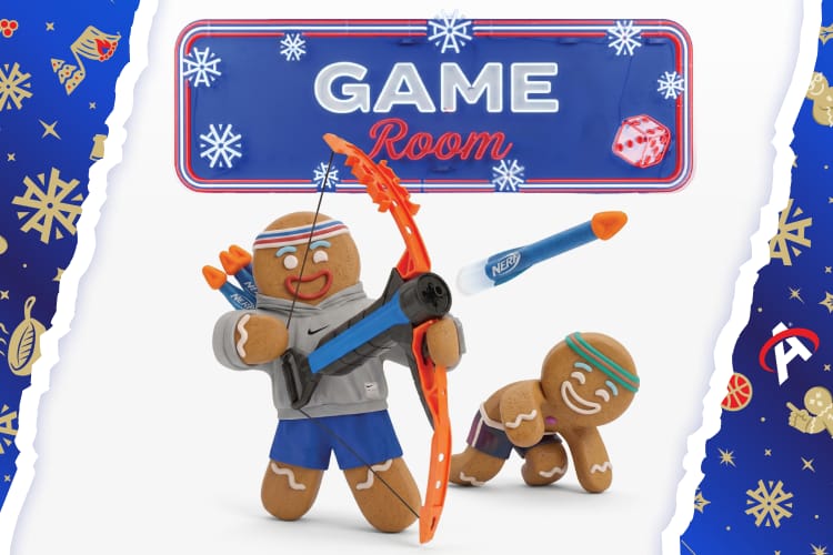 Holiday-themed Game Room banner with the text Game Room above two gingerbread cookie figures. One gingerbread character holds a toy bow and arrow while another crawls nearby. Blue decorative borders with snowflakes, ornaments, and holiday accents frame the image.