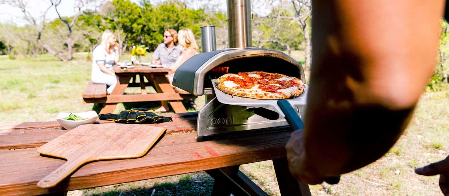 Man pulls pizza out of his portable pizza oven at group gathering