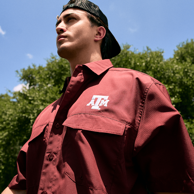 Person wearing a maroon Texas A&M collegiate button-down shirt outdoors against a blue sky.