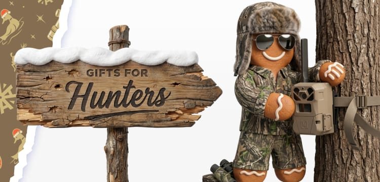 Holiday-themed Gifts for Hunters banner featuring a rustic wooden sign with the text Gifts for Hunters. Beside the sign, a gingerbread cookie figure dressed in camouflage-style clothing, aviator sunglasses, and a fur trapper hat stands next to a trail camera mounted on a tree. Decorative holiday accents and a brown patterned border frame the image.