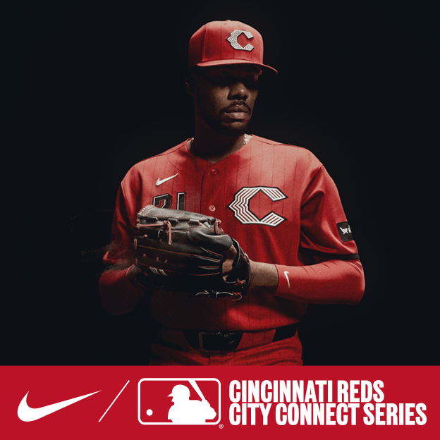 Professional baseball player wearing a red Cincinnati Reds City Connect jersey and cap, holding a mitt in dramatic studio lighting.