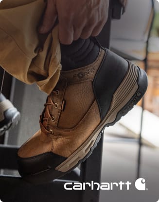Close-up of a tan Carhartt work boot with a black toe cap resting on equipment in a work setting.
