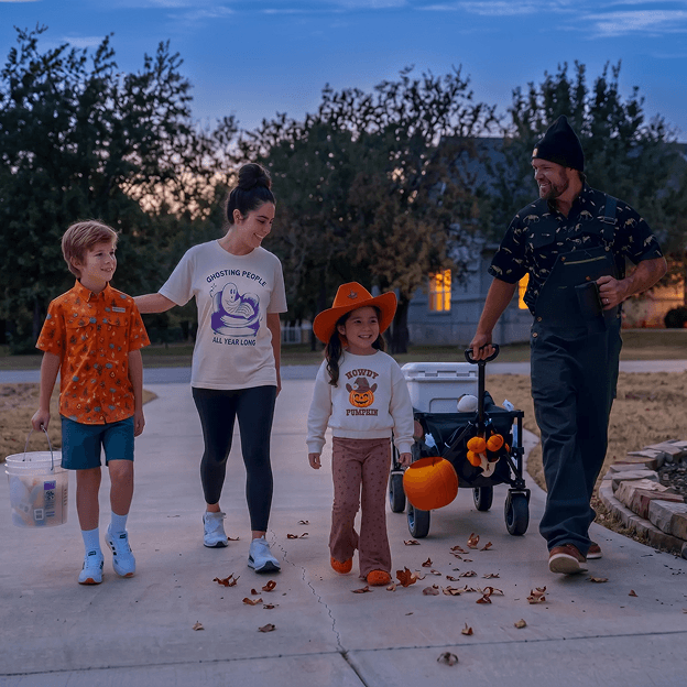 Promotional image showing a group walking outdoors at dusk carrying pumpkin buckets and wearing Halloween-themed apparel near a wagon and decorations.