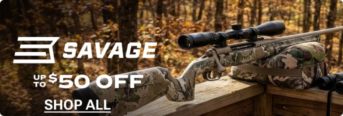 Savage rifle with mounted scope resting on a wooden shooting bench in a wooded outdoor setting.