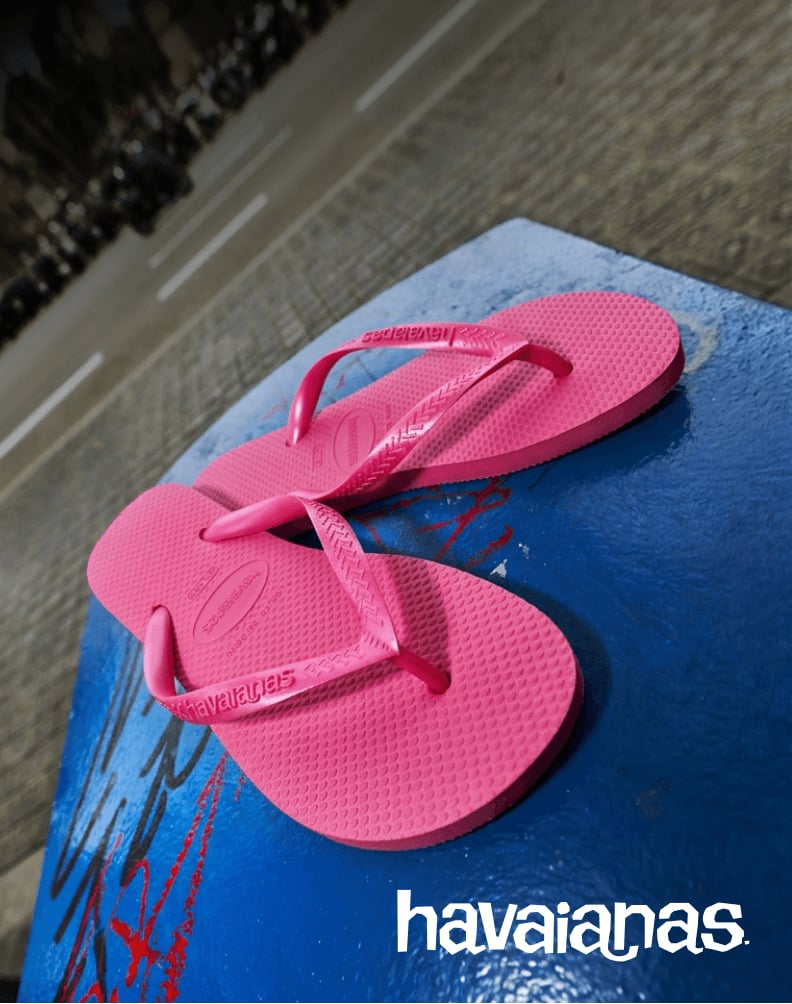 A pair of pink Havaianas flip-flops placed on a blue bench beside a street.