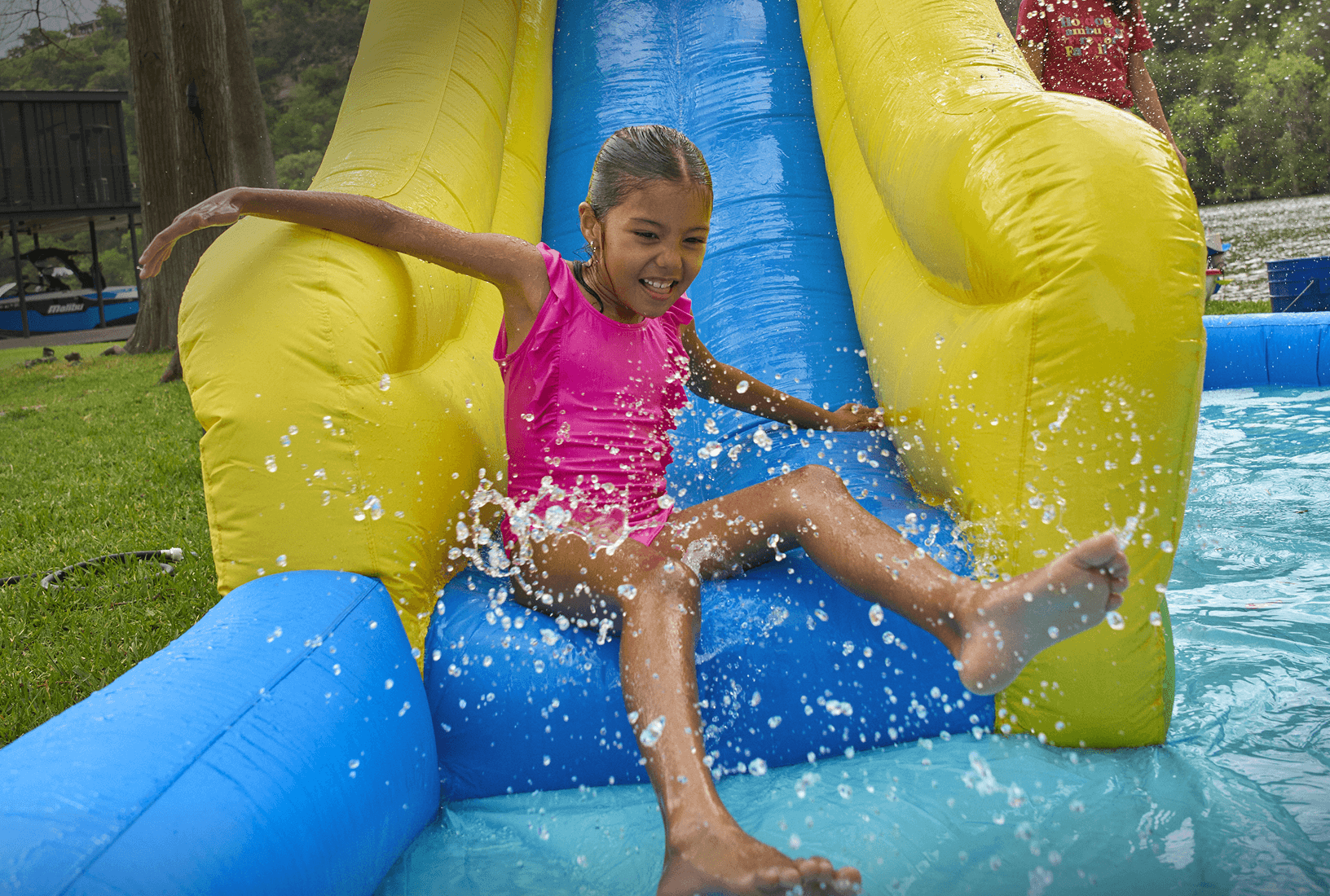 A girl splashes into a pool at the bottom of a bright yellow and blue inflatable water slide.
