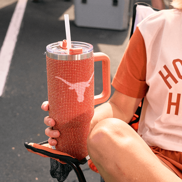 Insulated Texas Longhorns-branded tumbler with handle held beside casual collegiate apparel.