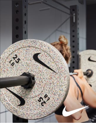 Close-up of a speckled Nike weight plate mounted on a barbell in a gym with a person lifting in the background.