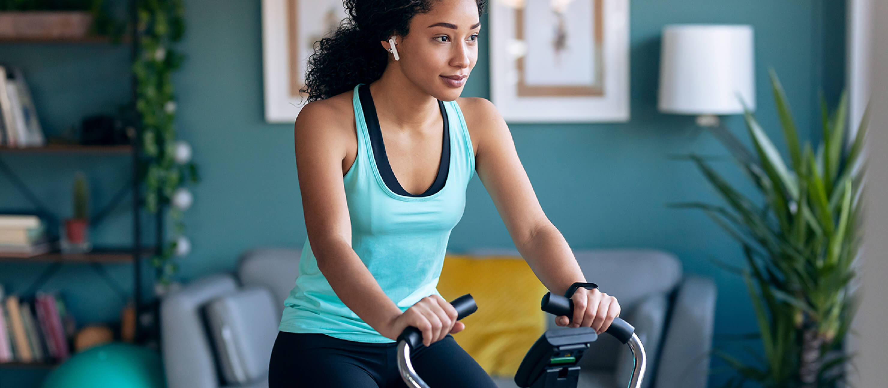 A woman in a light blue top pedals on her home exercise bike