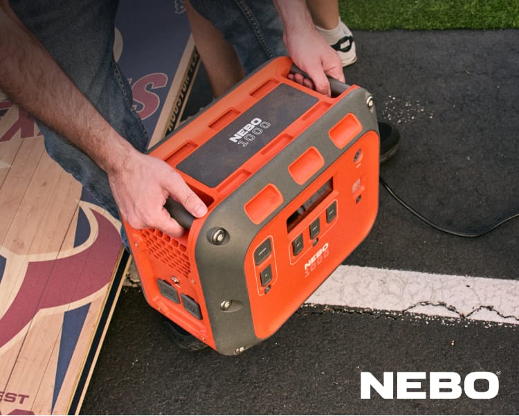 Portable power station being carried by a person, with the NEBO logo visible and a vehicle in the background.